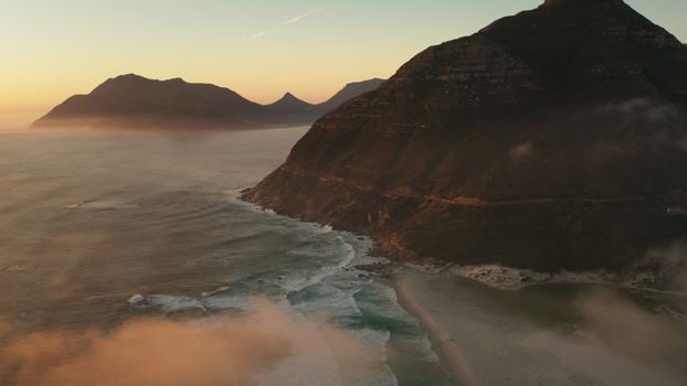 Stunning aerial view of mountains and ocean at twilight, with mist and waves.