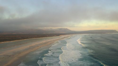 Free Discover a breathtaking aerial view of a serene coastal beach at sunrise, showcasing waves meeting sand. Stock Photo