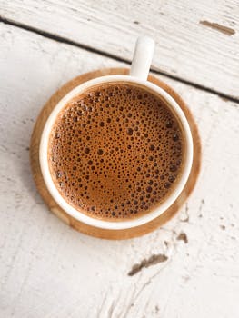 Top view of a frothy Turkish coffee in a white cup, set on a rustic wooden table. Perfect for coffee lovers.