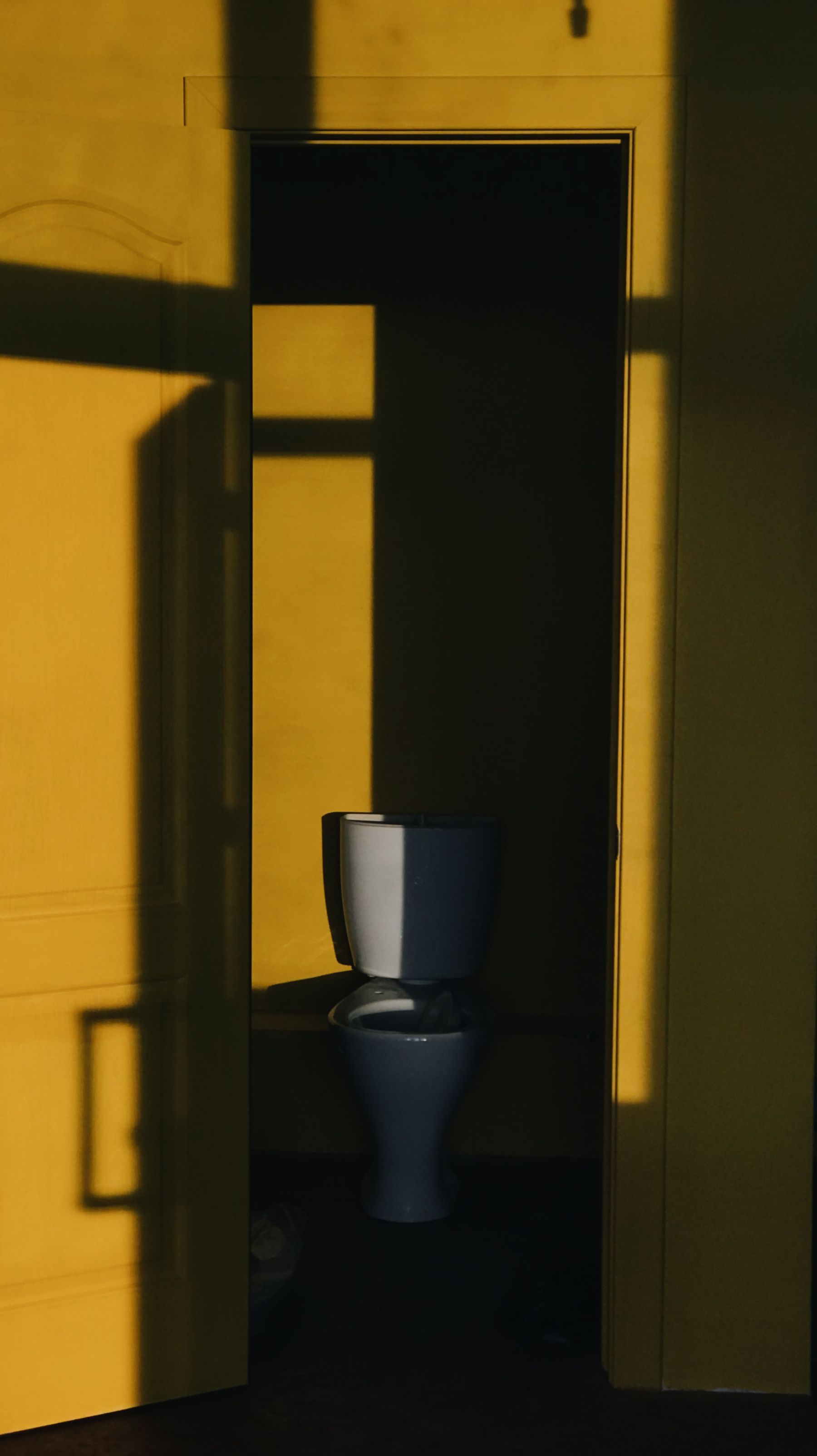 Minimal restroom interior with vivid yellow painted walls and strong shadow