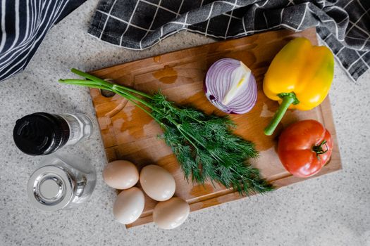 Top view of fresh vegetables, eggs, and herbs arranged on a wooden cutting board for cooking preparation.