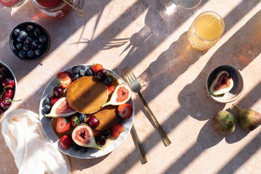 Flat lay of pancakes with fresh figs, berries, and juice on a sunny morning.