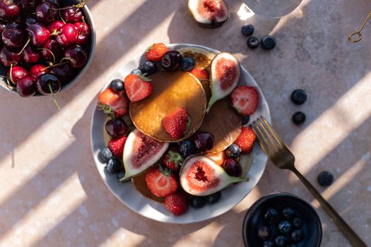 Top view of a delectable summer pancake breakfast with fruits like figs, strawberries, and blueberries.
