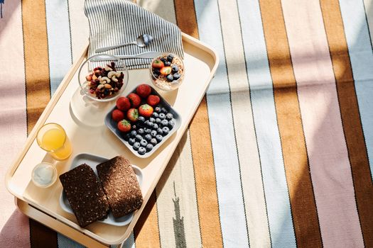 Top view of a healthy breakfast tray with fruits, bread, and juice on a striped tablecloth.