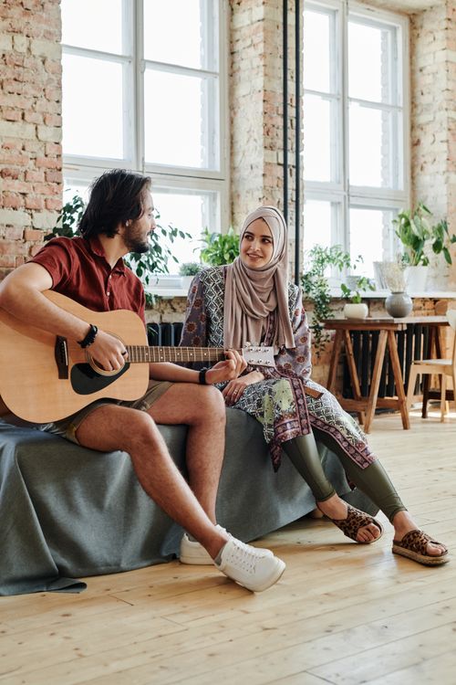 Free A couple sitting together indoors, with the man playing the guitar and the woman smiling, enjoying a romantic moment. Stock Photo
