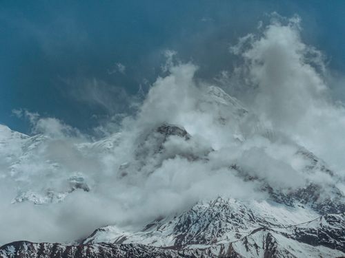 Free Spectacular view of snow-covered mountain peaks enveloped by clouds under a clear blue sky. Stock Photo
