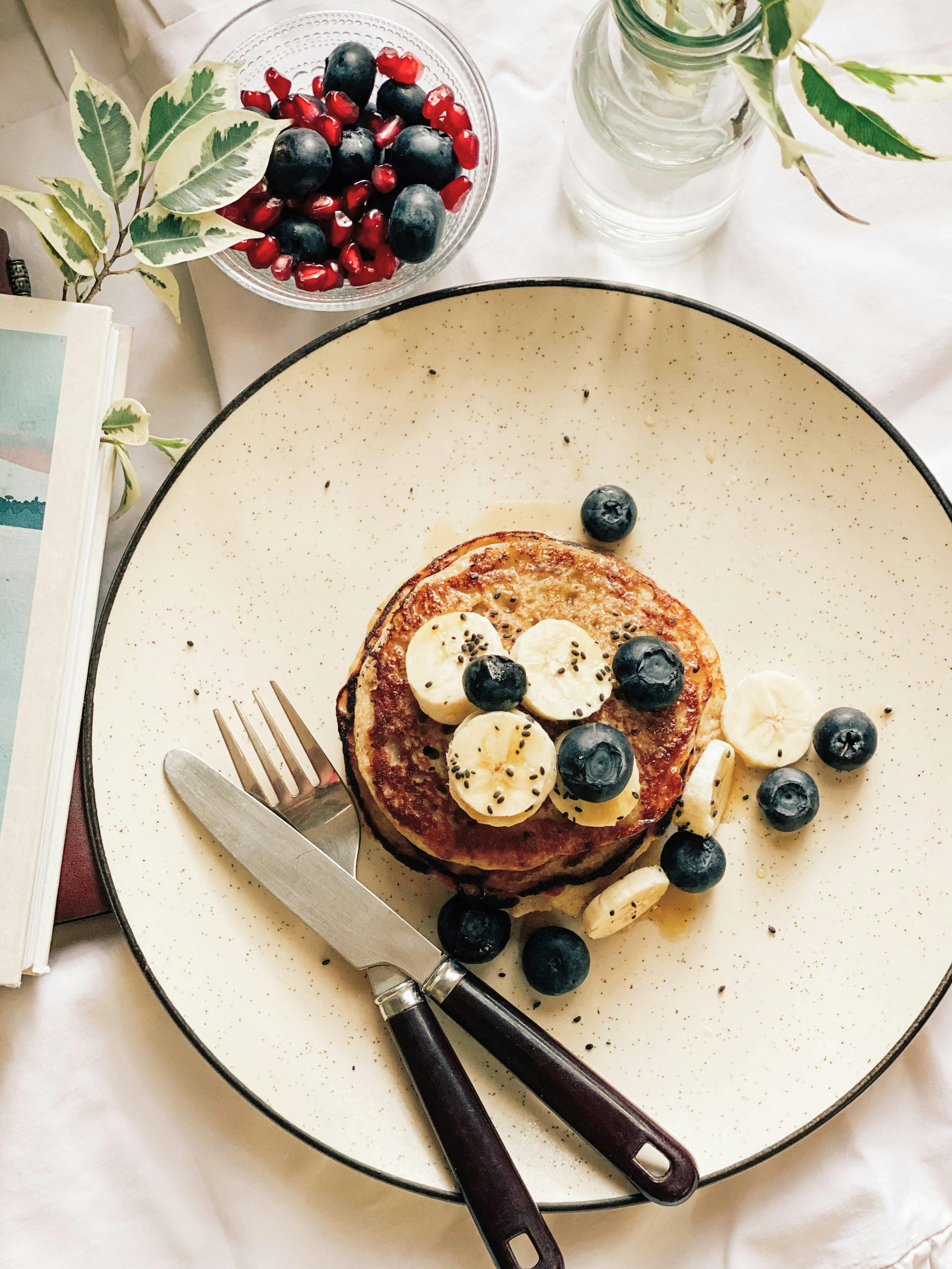 A close-up of pancakes topped with bananas and blueberries on a plate, perfect for a cozy breakfast setting.