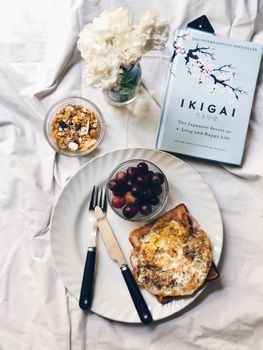 A cozy breakfast setup with granola, toast, grapes, and the book 'Ikigai'.