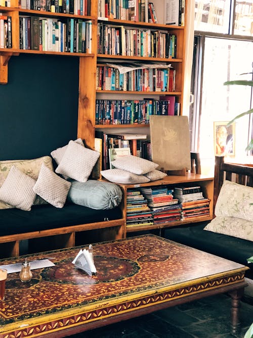 Free Stack of Books on a Brown Wooden Shelf Beside a Couch  Stock Photo
