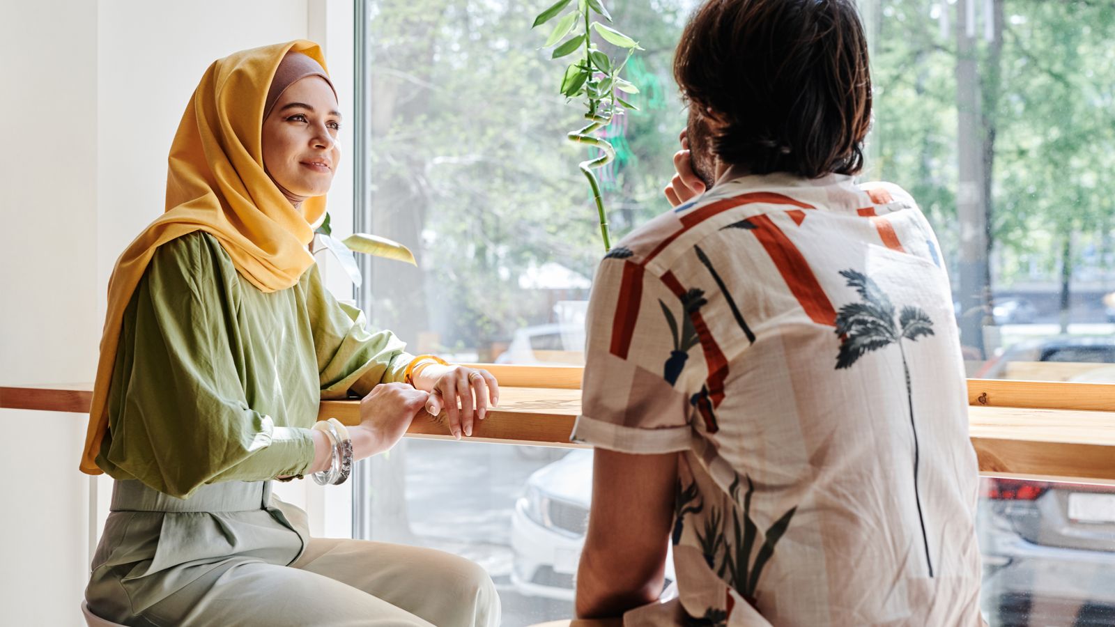 Two adults talking beside a bright café window