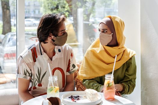 A young couple in masks sharing a meal in a cozy cafe, embracing togetherness.