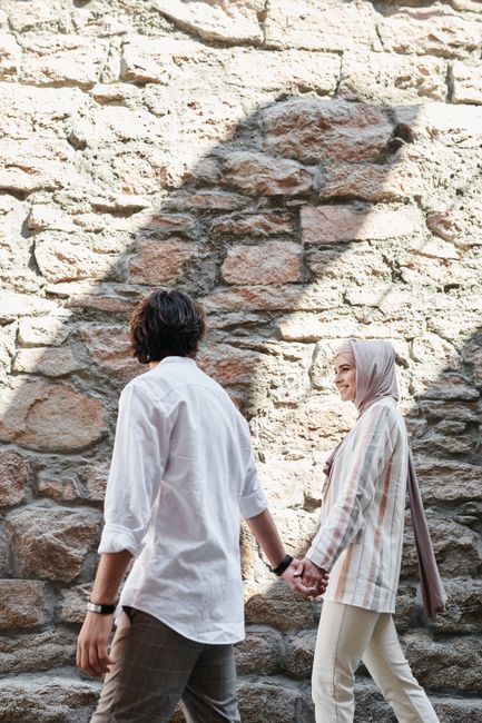 A couple walks hand in hand along a rustic stone wall, exuding togetherness in an outdoor setting.