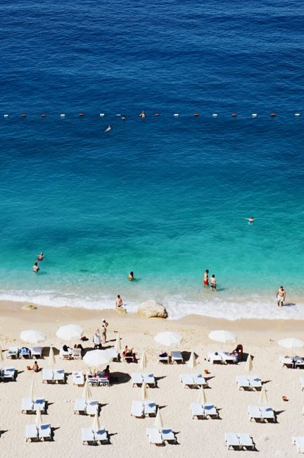 Relaxing summer scene on Antalya beach with sunbathers and swimmers.