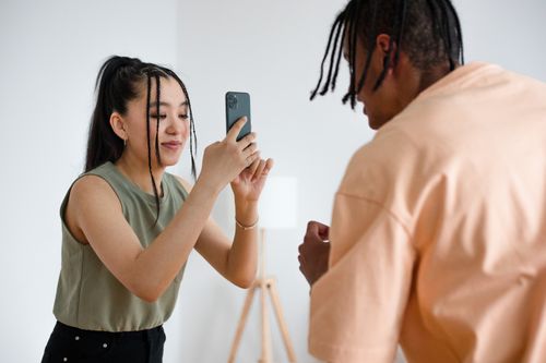 Free Woman capturing a photo of her friend using a smartphone indoors. Stock Photo