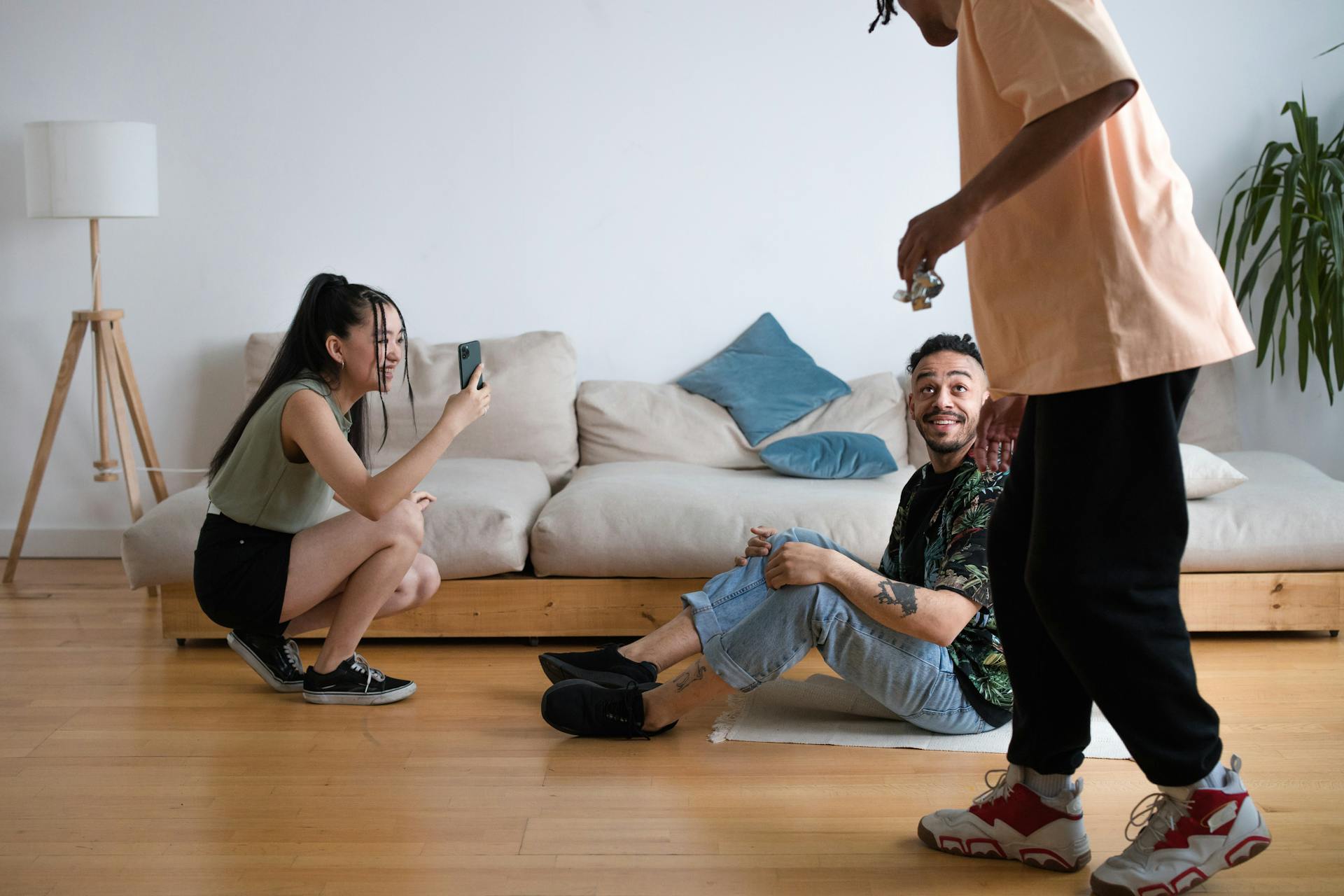 Three friends having fun filming a video indoors. A man and a woman use a smartphone while another man performs.