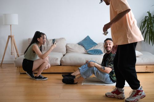 Free Three friends having fun filming a video indoors. A man and a woman use a smartphone while another man performs. Stock Photo