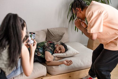 Free Two friends quietly film their sleeping friend for a prank video indoors. Stock Photo