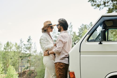 Free A romantic couple standing by a classic van in a lush outdoor setting, embracing each other. Stock Photo