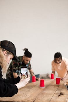 Group of friends playing a cup game while filming with smartphone indoors.