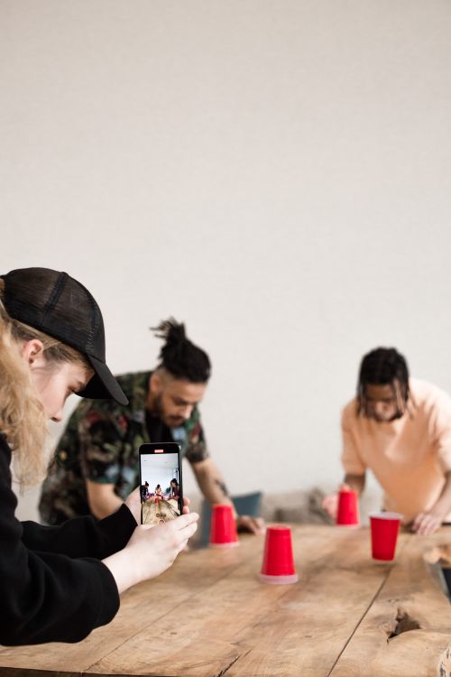 Free Group of friends playing a cup game while filming with smartphone indoors. Stock Photo