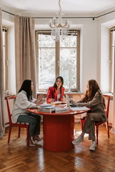 Three women engaged in a business meeting around a table in a stylish office setting.