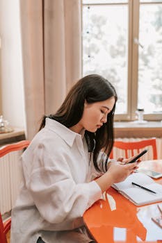 Focused young woman texting on smartphone at home office desk.