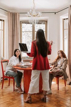 Three professional women in a business meeting, discussing strategies in a modern office setting.