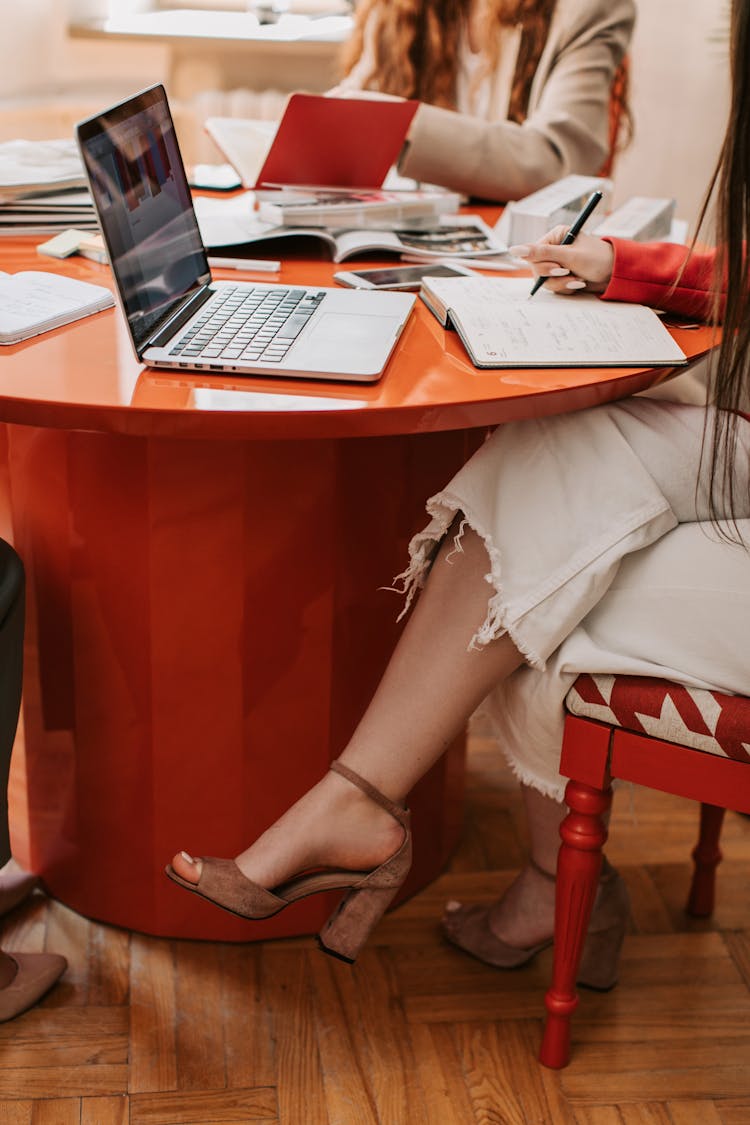 A Woman Writing On Notebook Near The Laptop On The Table