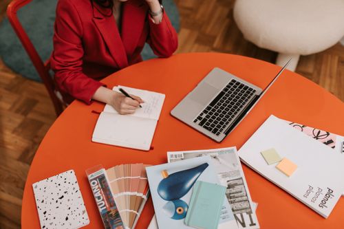 Free Woman writing in a notebook at a modern workspace with a laptop and documents. Stock Photo
