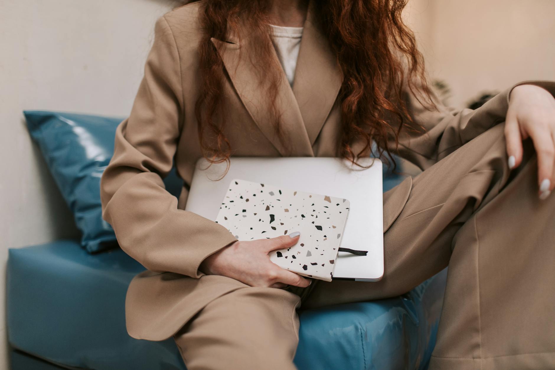Businesswoman sitting with a laptop on a sofa, holding a notebook indoors.
