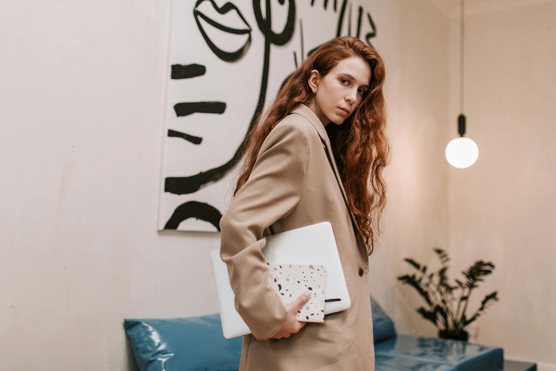 A confident woman in a business suit holding a laptop, posing indoors in a modern office environment.