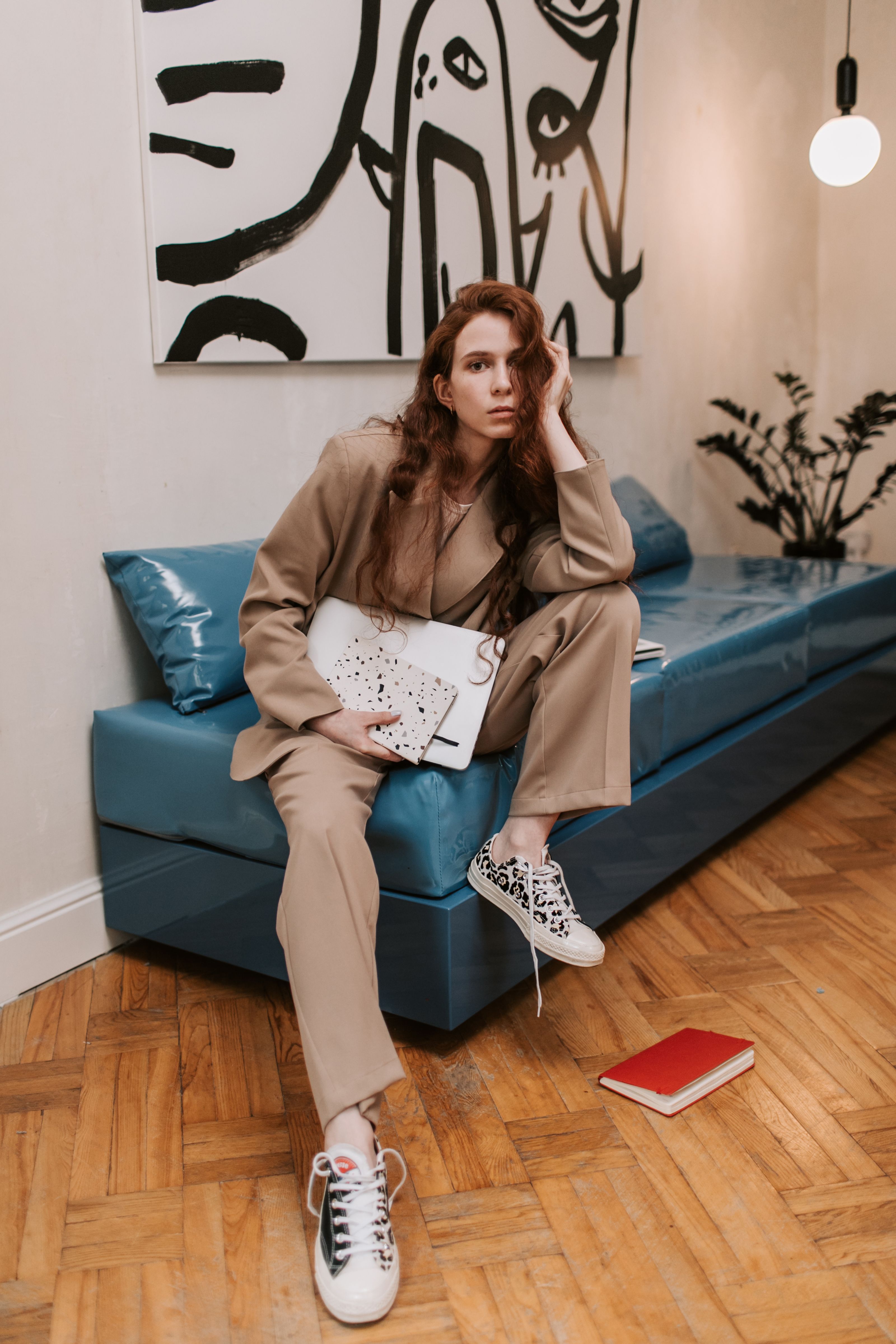 Stylish woman in beige suit sitting indoors with a notebook on a blue couch.