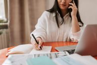 Woman in White Long Sleeve Shirt Holding Pen Writing on White Paper