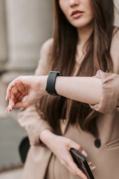 Fashionable woman looking at smartwatch while holding phone, capturing a modern lifestyle moment.