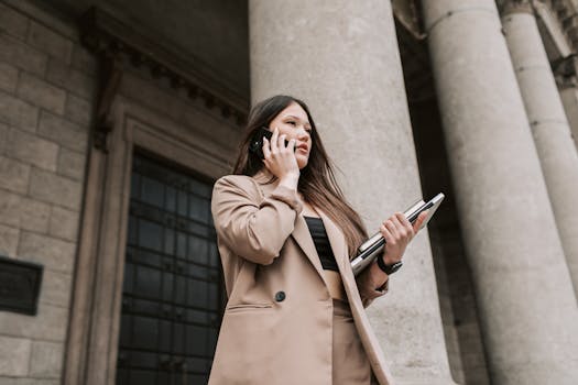 Confident businesswoman in beige coat on a phone call outside a classical building.