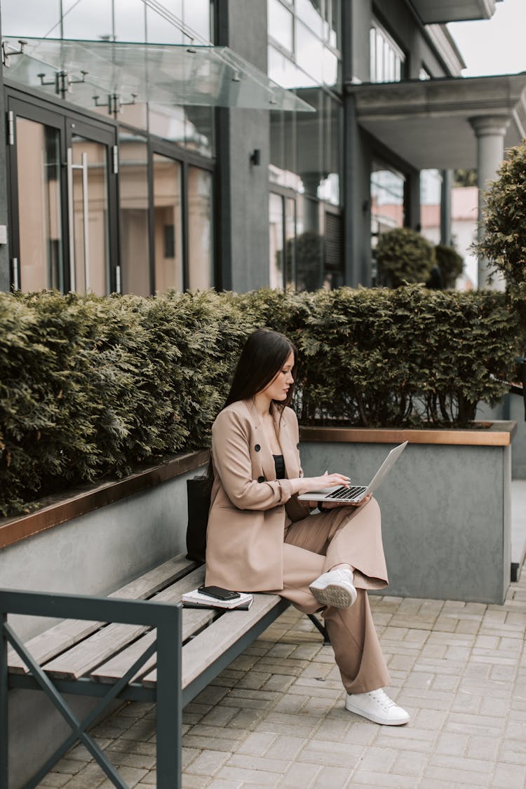 Woman In Brown Long Sleeve Shirt Sitting On A Bench Working On Her Laptop