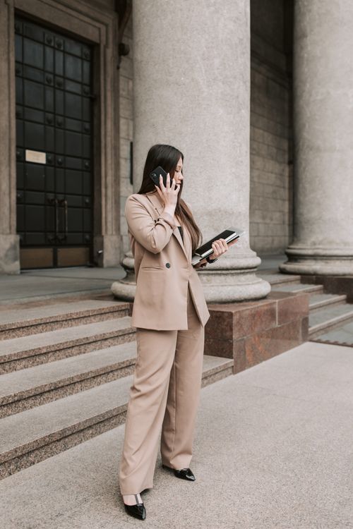 Free Professional woman in a beige suit stands outside an office building, taking a phone call. Stock Photo