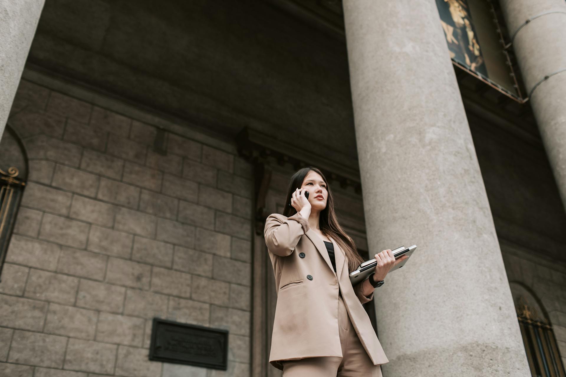 Businesswoman in stylish suit using smartphone outdoors by classic stone columns.