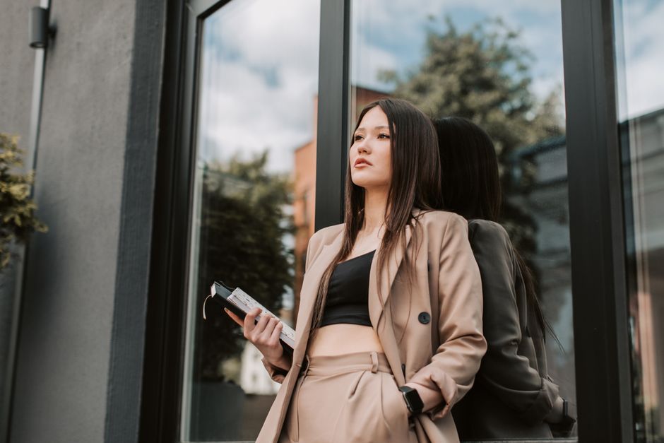 Stylish woman in brown suit posing confidently by a modern window.