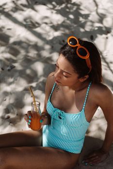 A woman enjoying a sunny day at the beach, sitting in the sand and sipping a refreshing drink.