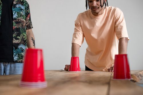 Free Two young men engaging in a fun cup game with red cups on a wooden table indoors. Stock Photo