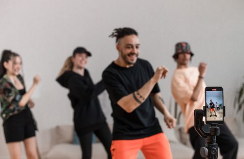 Free Group of friends dancing together indoors while recording on a smartphone. Energetic and joyful moment captured. Stock Photo