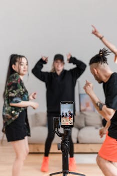 Energetic group of friends dancing and recording a video using a smartphone indoors.
