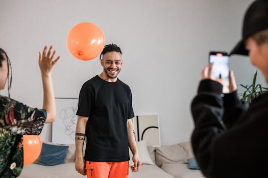 A cheerful group of adults enjoying a playful photo session indoors with orange balloons and a smartphone camera.
