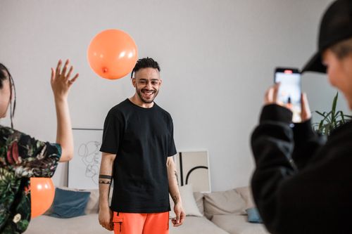 Free A cheerful group of adults enjoying a playful photo session indoors with orange balloons and a smartphone camera. Stock Photo