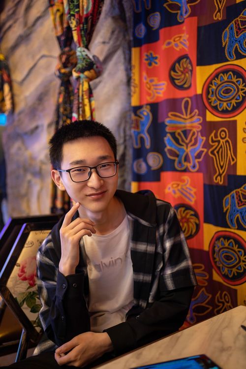 Free A young man wearing eyeglasses smiles while seated in a vibrant, colorful room. Stock Photo