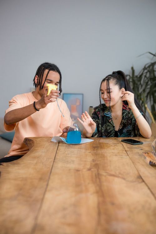 Free Two friends engaging in a fun science experiment with colorful liquids on a wooden table indoors. Stock Photo