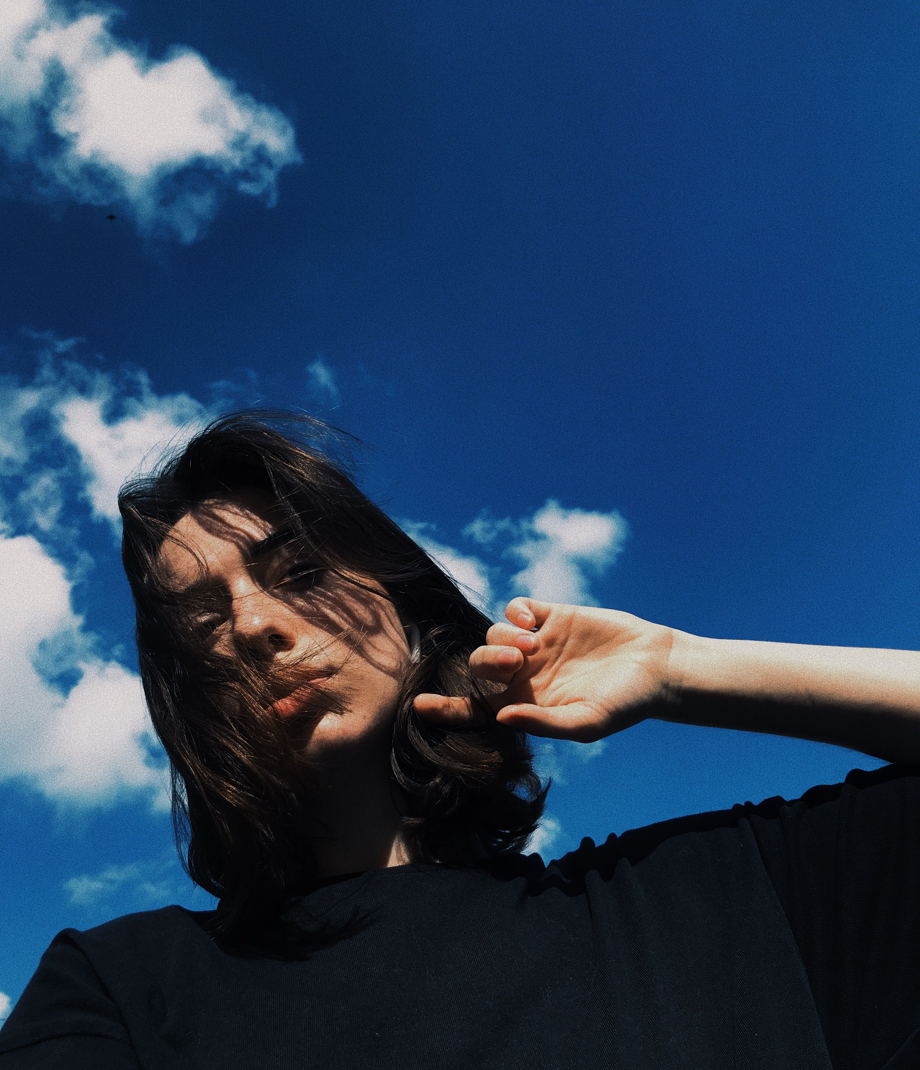 A woman poses outdoors with a serene expression under a vibrant blue sky.