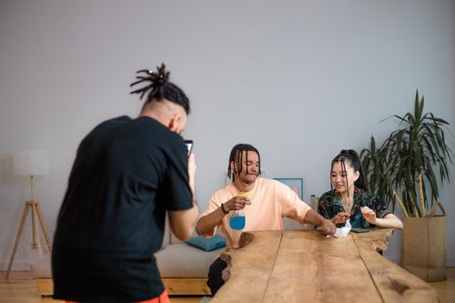 Free Two friends share a moment while being photographed indoors, engaging with a drink at a wooden table. Stock Photo