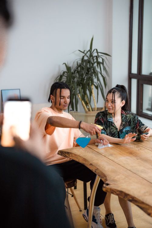 Free Two young adults cleaning a table, recording for TikTok indoors. Stock Photo